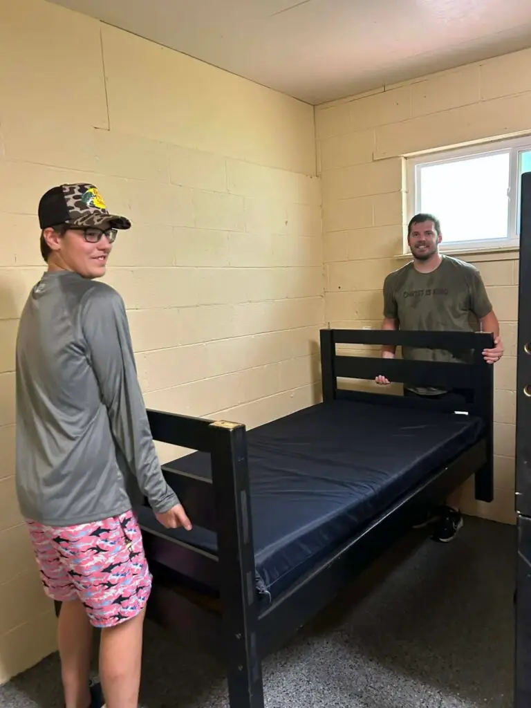 Volunteers setting up a freshly painted bunk bed with a new mattress in the remodeled Boys' Dorm